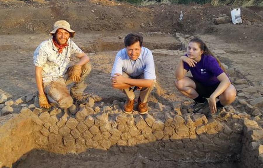 Team members pose near an excavated section of wall. Pictured on the right is incoming CIAMS MA student Dani Vander Horst.